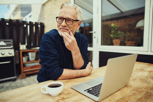 starszy mężczyzna siedzący na zewnątrz pijąc kawę i używając laptopa - senior adult computer men mature adult zdjęcia i obrazy z banku zdjęć