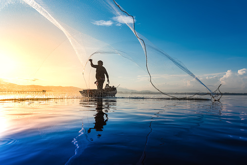 Silhouette of fishermen using coop-like trap catching fish in lake with beautiful scenery of nature morning sunrise. Beautiful scenery at Bang-Pra, Chonburi Province Thailand.