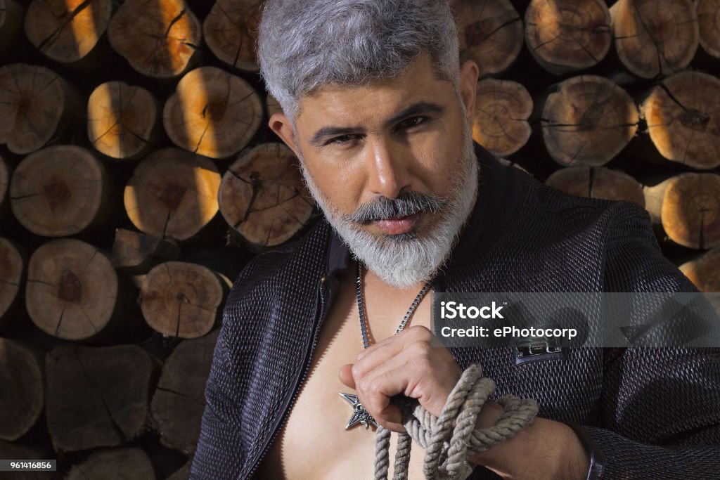 Man With White Hair And Beard In Black Shirt Sitting With Rope On Neck  Against A Log Background Stock Photo - Download Image Now - iStock