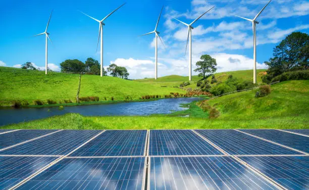 Solar panel and wind turbines farm on a green grass rolling hills against blue sky and white clouds in summer. Concept of renewable clean energy and sustainability business development.