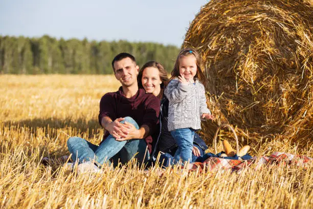 Happy young family with 2 year old girl next to hay bales in harvested field