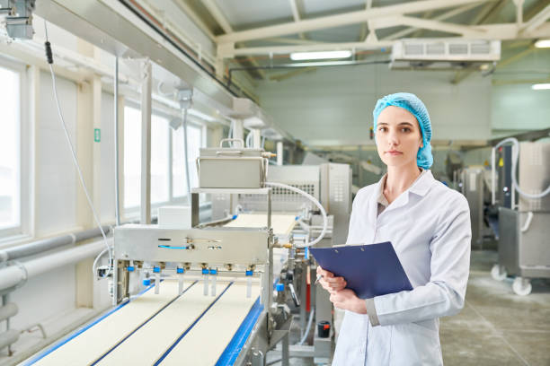 istock Serious confident quality control engineer in cap and lab coat holding clipboard and looking at camera while working at modern food factory 961453246
