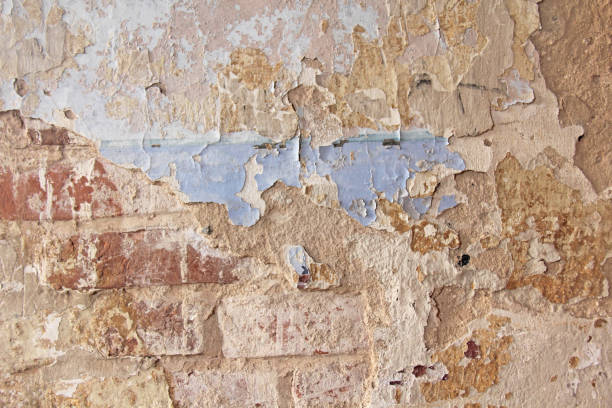 istock Old flaky white paint peeling off a grungy cracked wall. Cracks, scrapes, peeling old paint and plaster on background of old cement wall. An old cement stone wall as vintage cracked. Brick wall. 961453774
