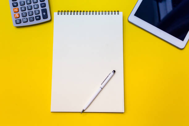 istock Yellow office desk table with  blank notebook, tablet and calculator. Top view 961454080