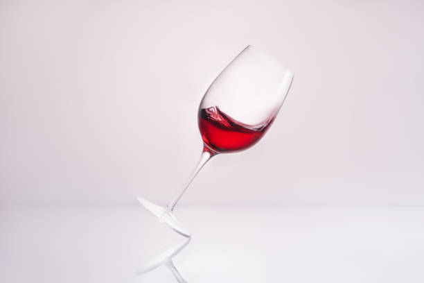 inclined wineglass with delicious red wine on reflective surface and on white - wineglass red wine wine liquid imagens e fotografias de stock