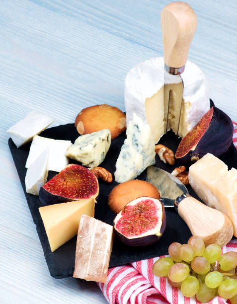 Gourmet Cheese Plate Gourmet Cheese Plate with Brie, Parmesan, Roquefort, Camembert and Fruits with Biscuits on Slate Plate with Napkin closeup on Wooden background plate fig blue cheese cheese stock pictures, royalty-free photos & images