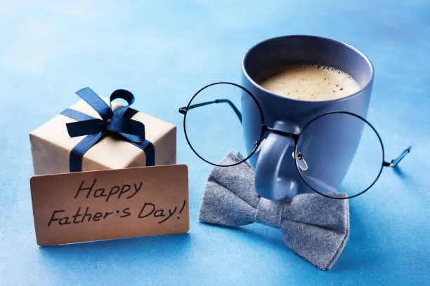 Creative breakfast on Happy Fathers Day with gift box, funny face from cup of coffee, eyeglasses and bowtie. Vintage style.