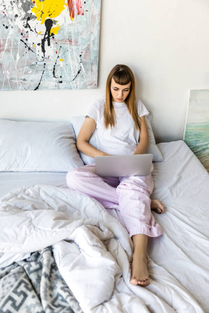 istock focused young woman using laptop while resting in bed in morning at home 961516442
