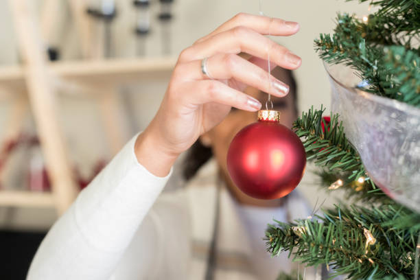 ornement de noël étant accroché sur l’arbre par femme méconnaissable - christmas ball christmas ornament human hand photos et images de collection