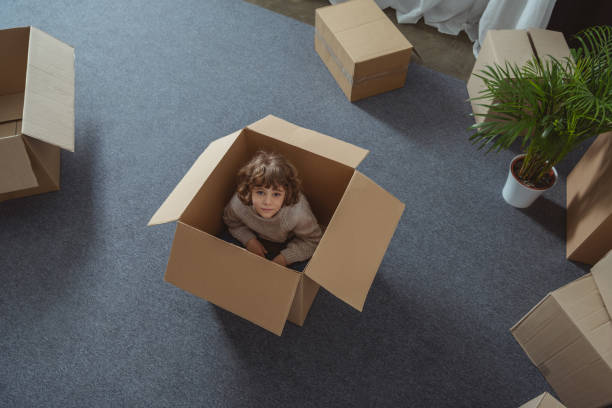 istock high angle view of little boy sitting in box and looking at camera during relocation 961526076