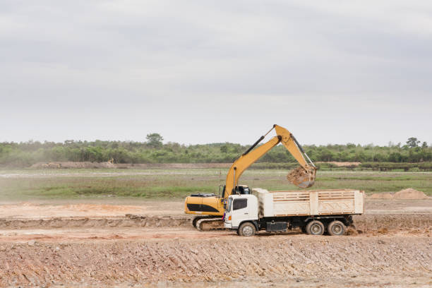 istock Yellow excavator machine loading soil into a dump truck at construction site 961526378
