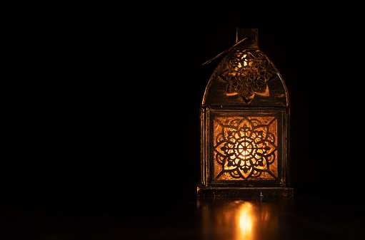 Traditional ornamental arabic lantern with a burning candle in dark studio setting. Festivel greeting card for Ramadan Kareem and Ramadan Mubarak. Dubai, UAE.