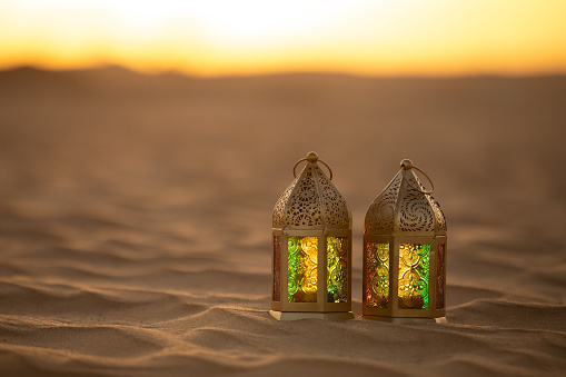 Traditional ornamental arabic lantern with a burning candle in desert during sunset. Festivel greeting card for Ramadan Kareem and Ramadan Mubarak. Dubai, UAE.