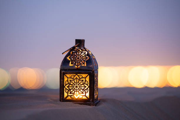 Traditional ornamental arabic lantern with a burning candle in desert after sunset during blue hour. Festivel greeting card for Ramadan Kareem and Ramadan Mubarak. Dubai, UAE.