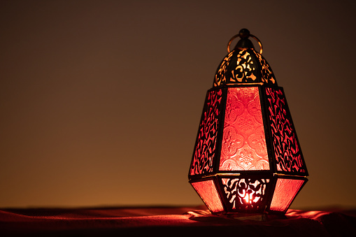 Traditional ornamental arabic lantern with a burning candle in desert after sunset during blue hour. Festivel greeting card for Ramadan Kareem and Ramadan Mubarak. Dubai, UAE.