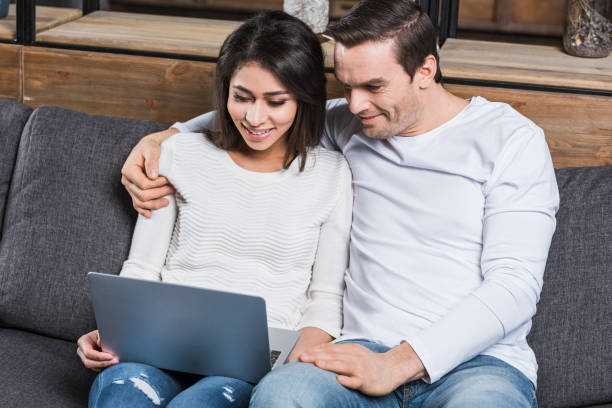 istock smiling multiethnic couple using laptop together while sitting on sofa at home 961531356