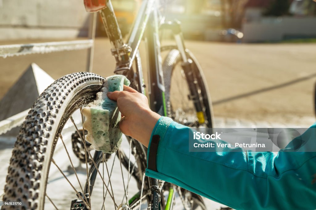 rueda de bicicleta con esponja de limpieza de la mano de la mujer. - Foto de stock de Bicicleta libre de derechos