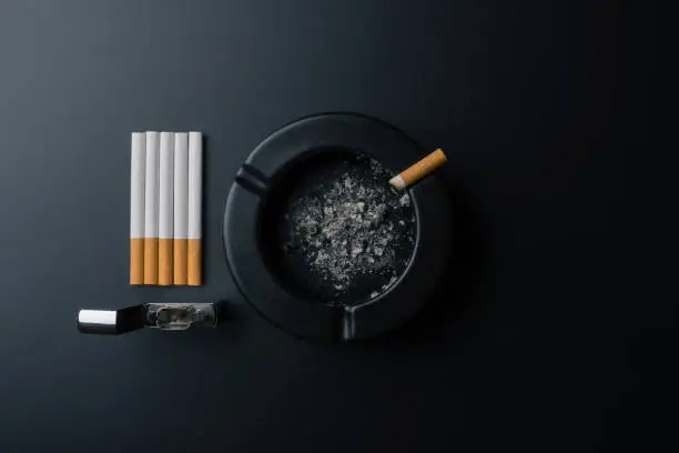 Photo of cigarettes, chrome lighter and black ceramic ashtray