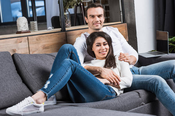 istock happy multiethnic couple smiling at camera while resting together on sofa at home 961540036
