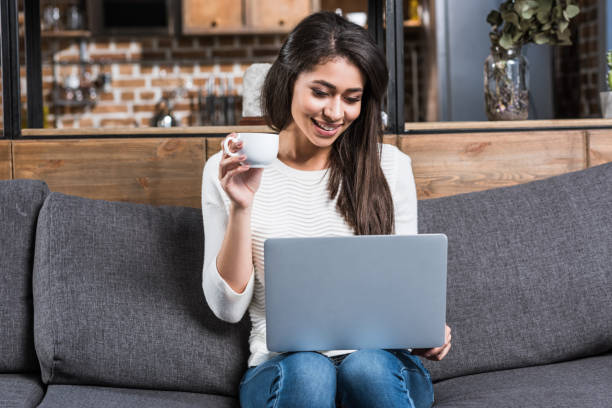 istock happy african american girl using laptop and drinking coffee on couch 961542842