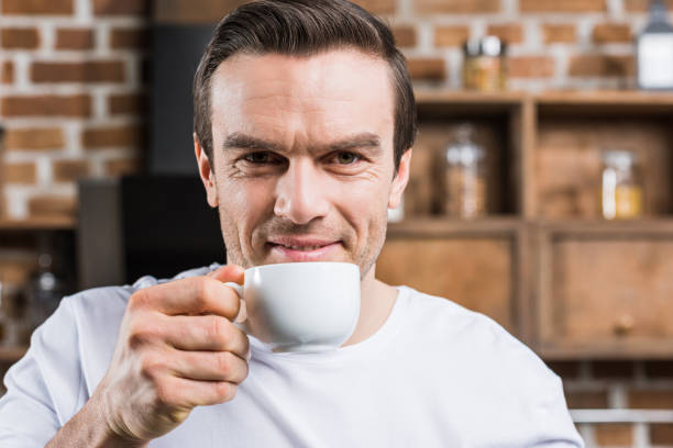 istock handsome man drinking coffee and smiling at camera at home 961543364