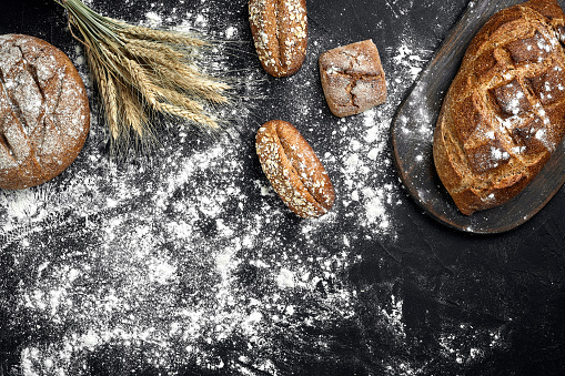 Different bread with flour and spikelets of wheaton black background. Top view. Still life. Flat lay