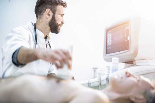 Doctor examining male mature patient's chest with ultrasound.