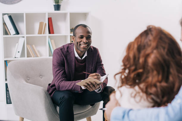 sonriendo el psiquiatra americano africano hablando con pareja joven - profesional de salud mental fotografías e imágenes de stock