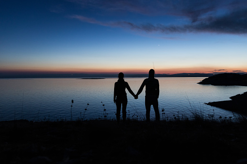 Silhouette of couple holding hands at sunset