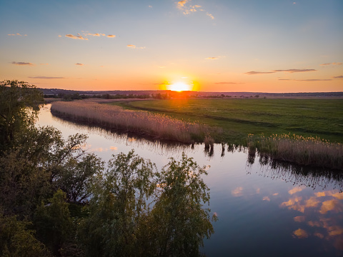 The calm surface of the river, orange sunset, green fields and meadows in a quiet warm summer evening