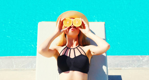 vacaciones de verano - soleado retrato de mujer en naranjas de las manos y oculta sus ojos en el fondo de piscina de agua azul - cama solar fotografías e imágenes de stock