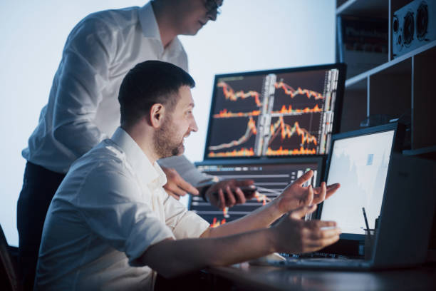 istock Team of stockbrokers are having a conversation in a dark office with display screens. Analyzing data, graphs and reports for investment purposes. Creative teamwork traders 961611002
