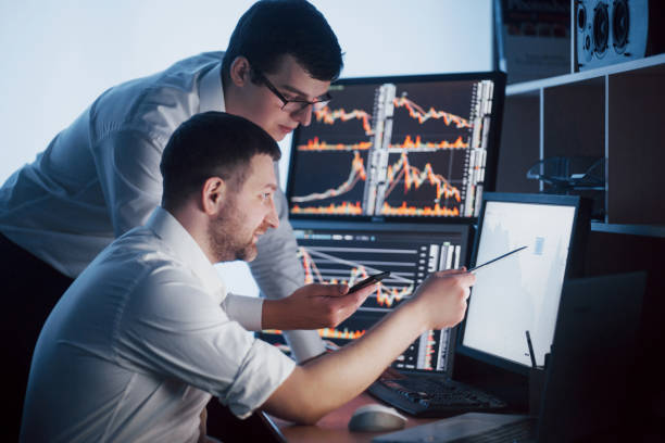 istock Team of stockbrokers are having a conversation in a dark office with display screens. Analyzing data, graphs and reports for investment purposes. Creative teamwork traders 961611042
