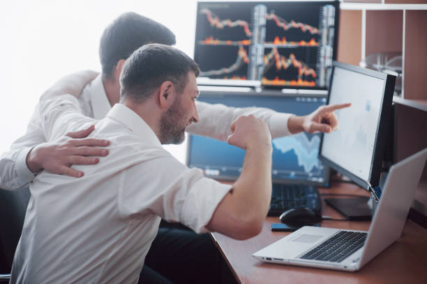 istock Team of stockbrokers are having a conversation in a dark office with display screens. Analyzing data, graphs and reports for investment purposes. Creative teamwork traders 961613110