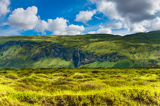 Panoramic view of illuminated grass field and waterfall on Iceland, summer time, wide angle, sunny day, South Iceland