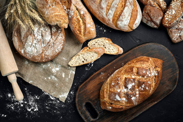 istock Fresh bread, wooden board and cutting knife on black table 961623066
