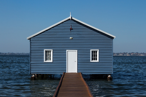 Blue wooden boatshed surrounded by water against clear blue sky
