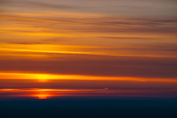 istock Big red sun circle rises out from behind dark horizon on background varicolored clouds of warmly shades. Beautiful background of dawn on picturesque cloud sky. 961634478