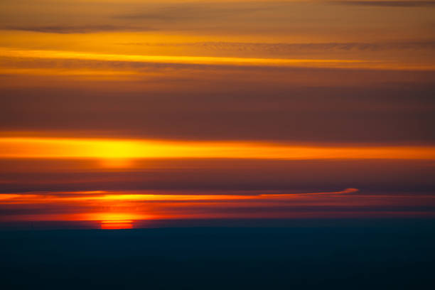 istock Big red sun circle rises out from behind dark horizon on background varicolored clouds of warmly shades. Beautiful background of dawn on picturesque cloud sky. 961634482