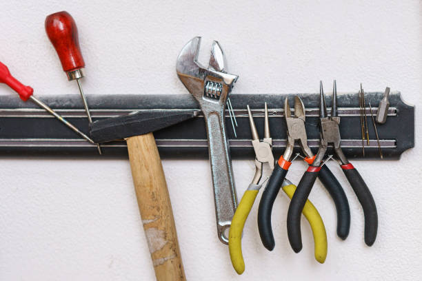 Set of tanner tools close-up. An awl, screwdriver, hammer, wrench, pliers and wire cutters hang on magnetic holder.