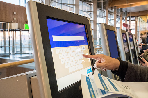 Tourist hand touching display at self-service transfer machine, buying airplane or train tickets at automatic device at international airport
