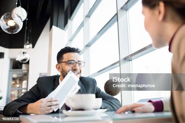 Positive Successful Young Arabian Businessman Excited About Business Trip And Showing Airline Tickets To Colleague In Cafe Stock Photo - Download Image Now