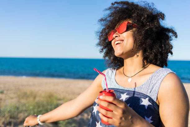 istock Carefree african woman drinking red can on beach 961709088