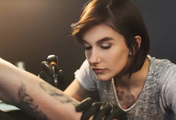 A professional tattooer artist doing picture on man hand by machine. Tattoo art on body. Equipment for making black ink from a jartattoo art.