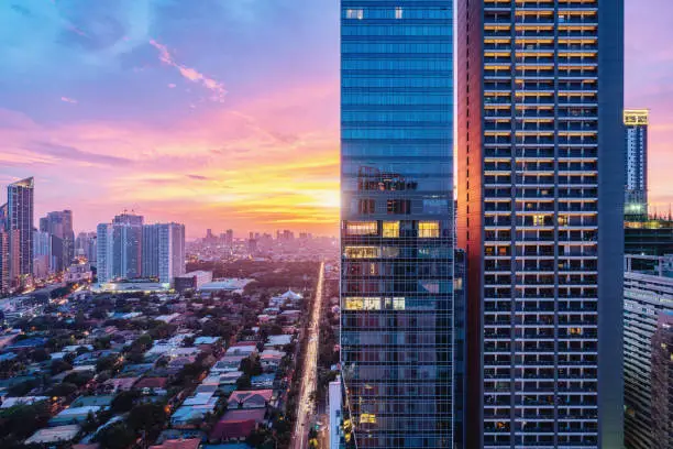 Colorful vibrant sunset over Makati in Downtown Manila. Aerial view along city road towards the sun. Modern skyscrapers in the foreground. Makati, Manila, Philippines, Asia.