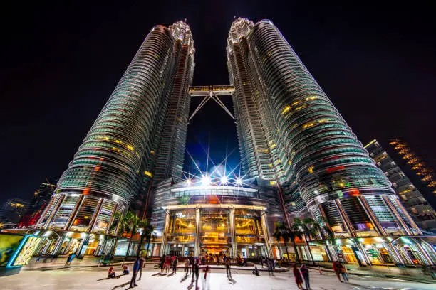 View from the entrance up to the iconic illuminated Petronas Twin Towers in Downtown Kuala Lumpur at Night. Ultra Wide Angle Architecture Shot. Kuala Lumpur, Malaysia, Asia.