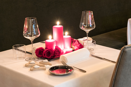 Romantic candlelit table setting for two with a centrepiece of burning red candles and fresh flowers set with matching red dinnerware and elegant glasses for Valentines