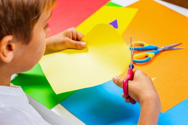 istock Child cutting colored paper with scissors at the table 961719254