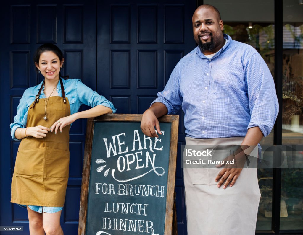 Cheerful business owners standing with open blackboard Small Business Stock Photo