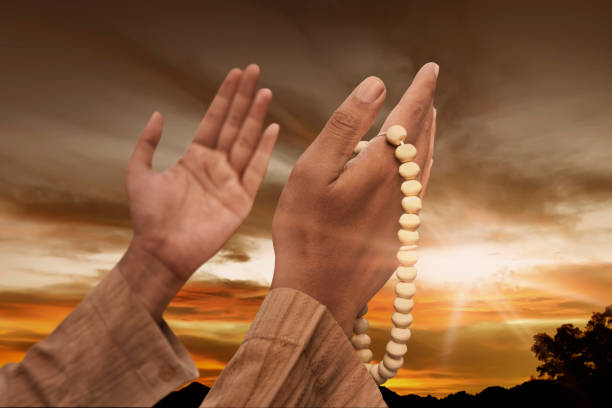 Muslim man praying with prayer beads at sunset